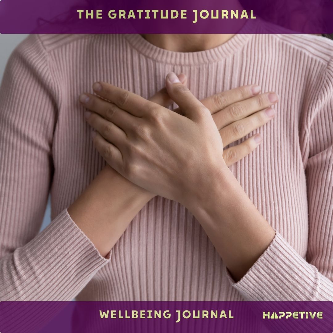 A women wearing a pink sweatshirt with hands crossed on her heart, stating gratitude journal as a wellbeing activity - Happetive