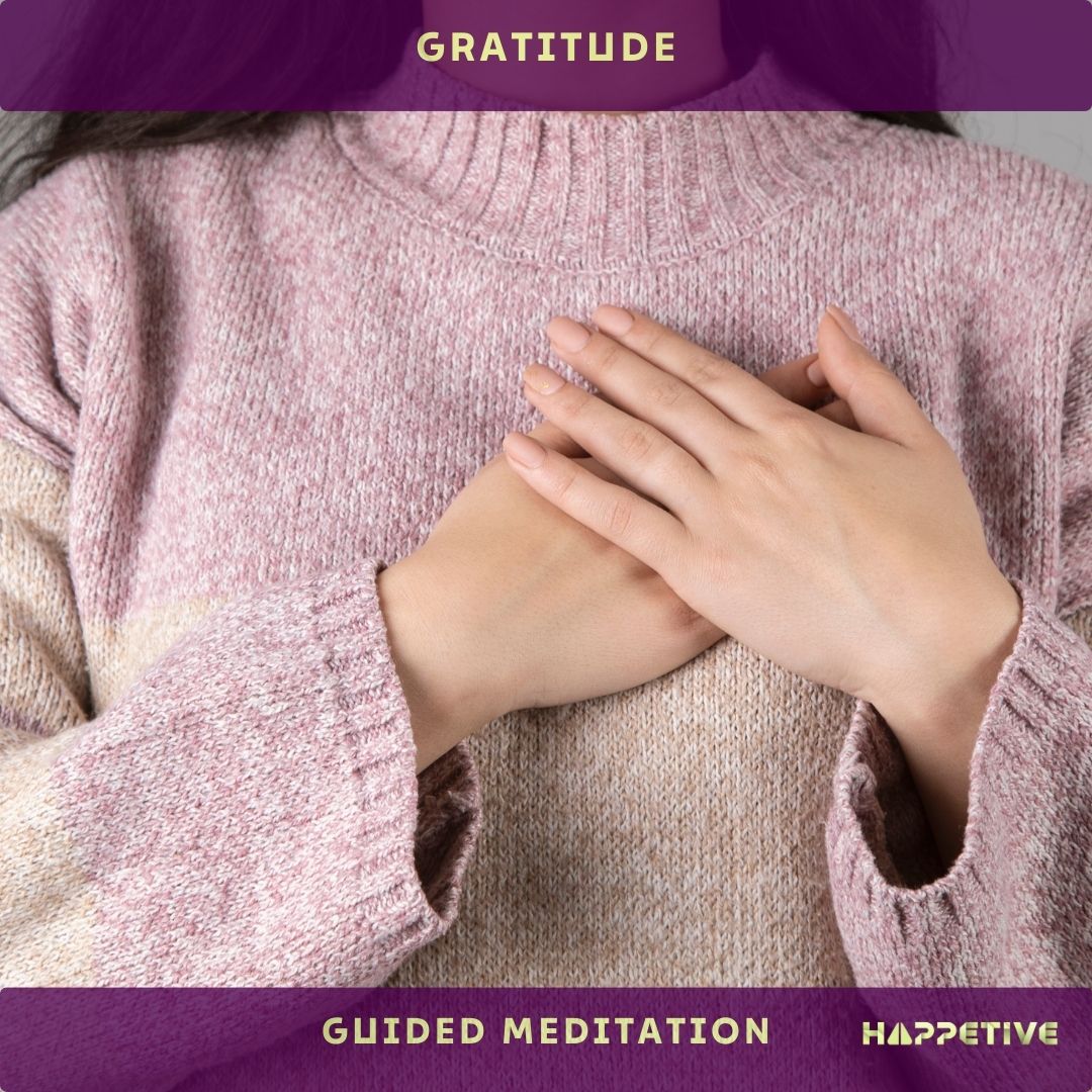 A women waring a pink sweater with both hands on her heart and embracing gratitude with guided meditation - Happetive